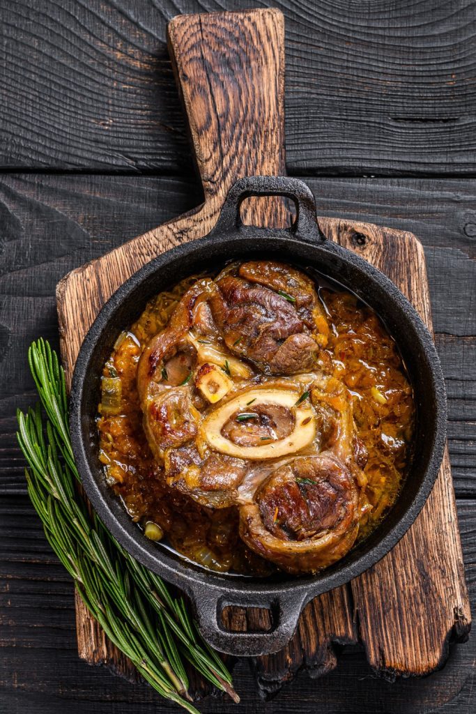 Mexican Osso Buco in a cast iron skillet on a wooden board, garnished with rosemary.