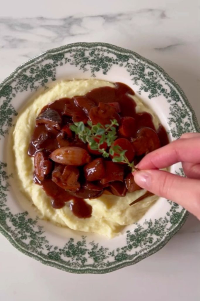 Slow Cooker Mushroom Bourguignon on mashed potatoes, with a hand garnishing it with thyme.