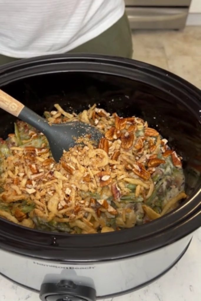 Green Bean Casserole in a slow cooker topped with fried onions and pecans.