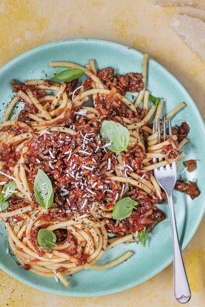 Bored of Lunch Slow Cooker Spaghetti Bolognese on a green plate with a fork, showing basil leaves and grated cheese.