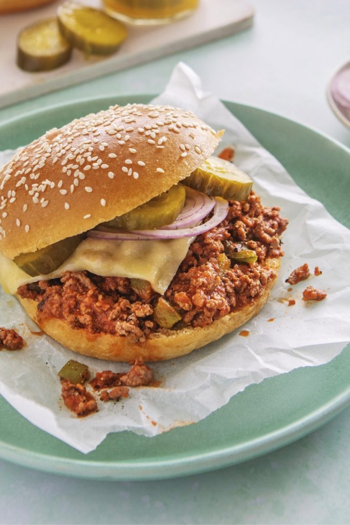 Bored of Lunch Slow Cooker Sloppy Joes on a sesame bun with pickles and cheese.