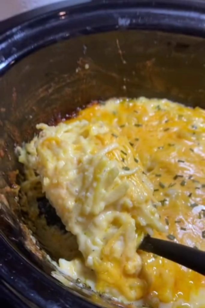 A spoonful of Cracker Barrel Hashbrown Casserole with melted cheese from a slow cooker.