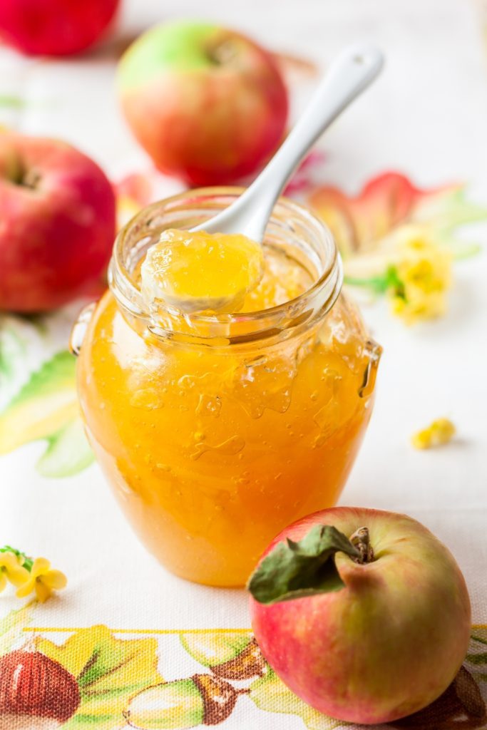  Jar of apple jam with a spoon surrounded by apples.