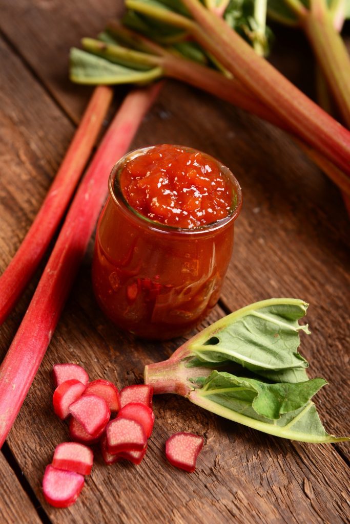 Jar of rhubarb jam with fresh rhubarb stalks and leaves.