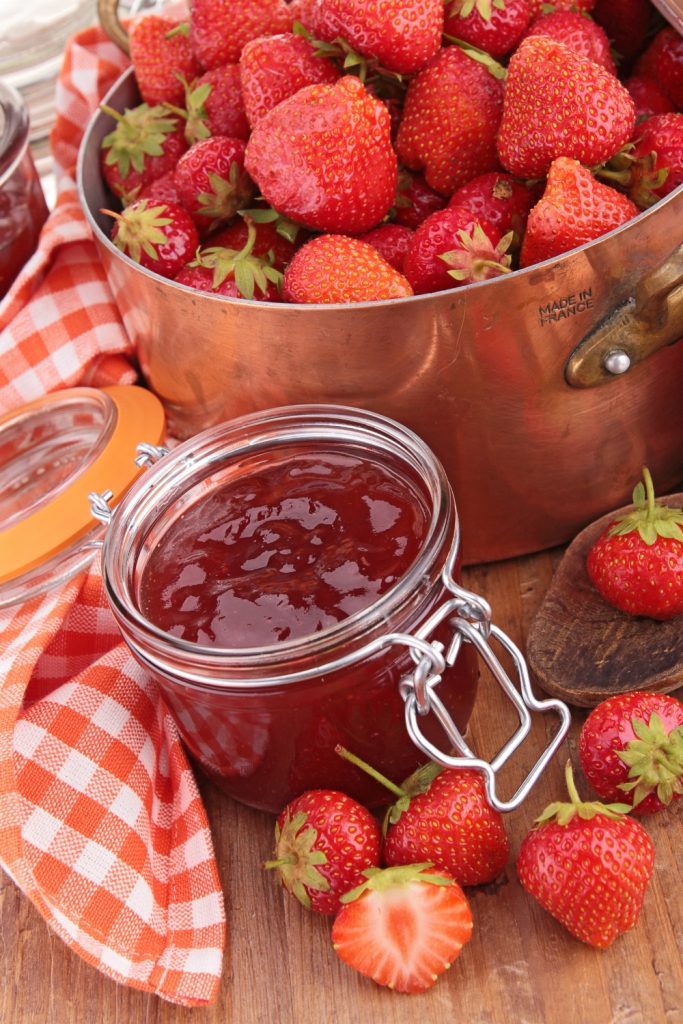 Jar of strawberry jam and a pot of fresh strawberries.