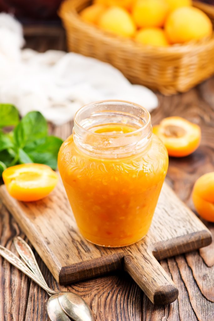 Bowls of apricot jam with fresh apricots and leaves on a dark background.