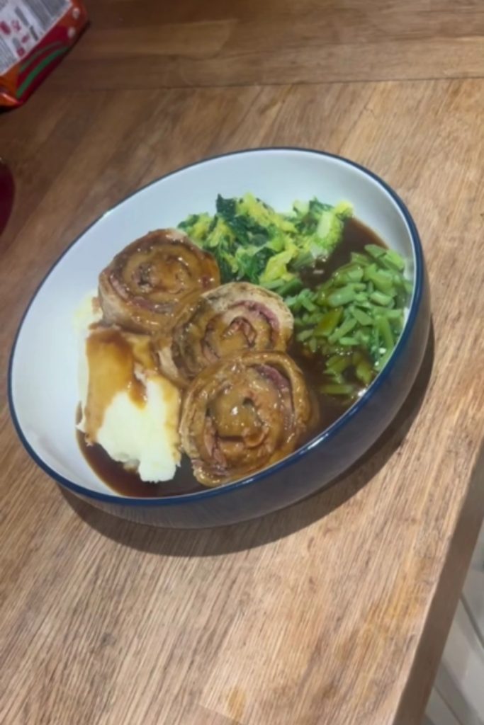 Slow Cooker Bacon and Onion Pudding with mashed potatoes, green beans, and cabbage, on a wooden table.