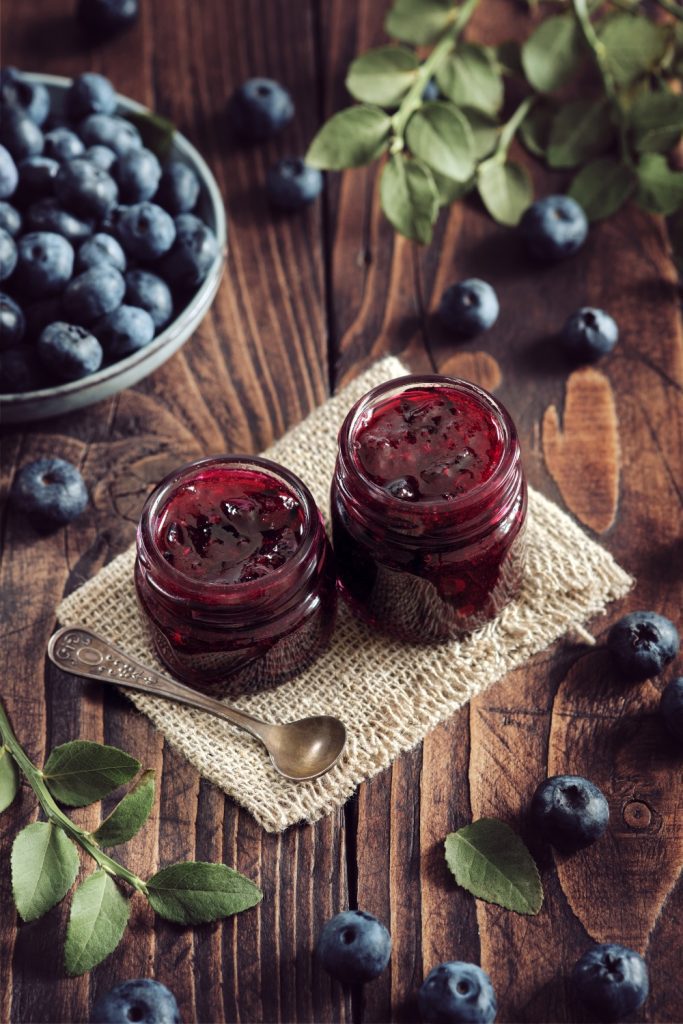 Jar of Slow Cooker Blueberry Jam with fresh blueberries and a green leaf.