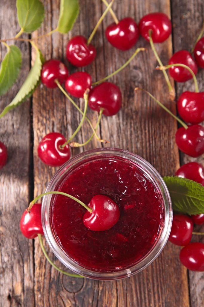 Jar of Slow Cooker Cherry Jam with fresh cherries on a wooden table.