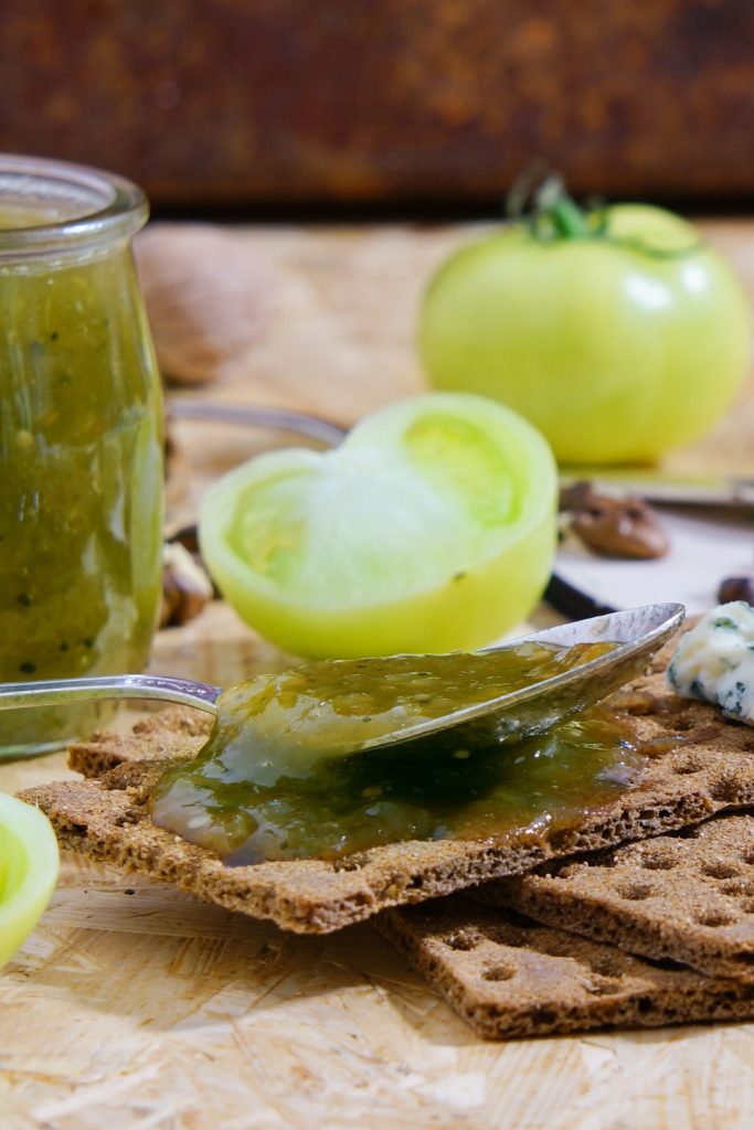 Jar of Slow Cooker Green Tomato Jam with a green checkered cloth lid and a wooden spoon.