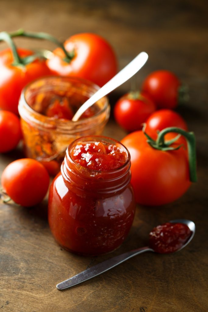 Slow Cooker Tomato Jam in a jar with a spoon, with fresh tomatoes nearby.