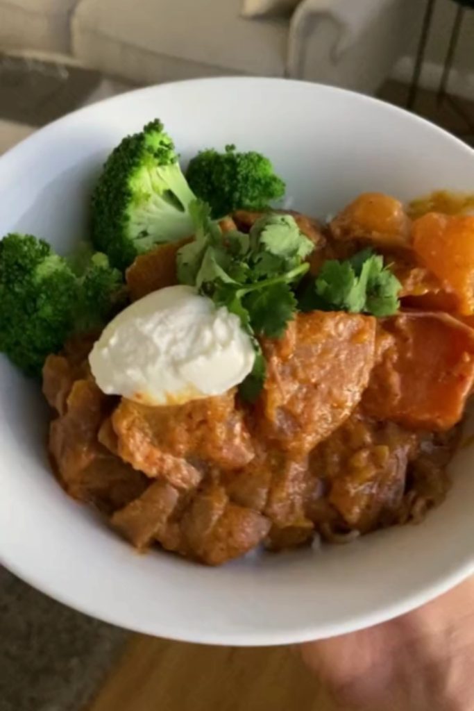 Lamb Massaman Curry in a bowl with broccoli, a dollop of yogurt, and cilantro on top.