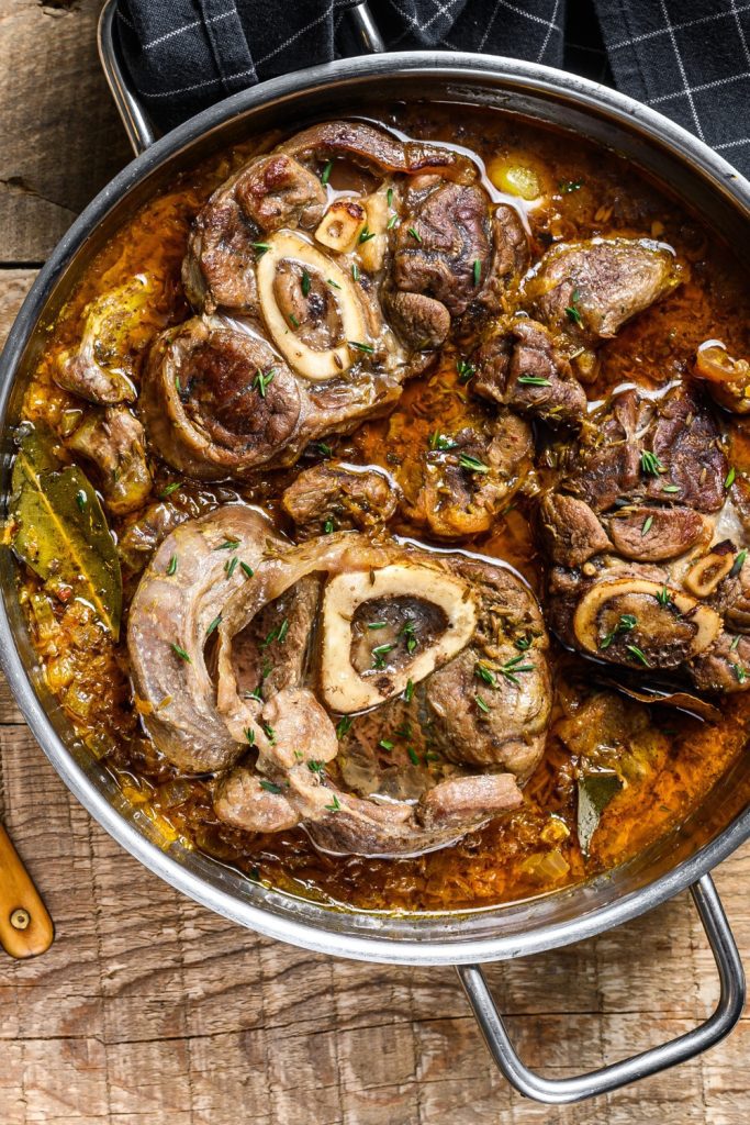 Mexican Osso Buco in a metal pan with a rich sauce and garnished with fresh herbs.