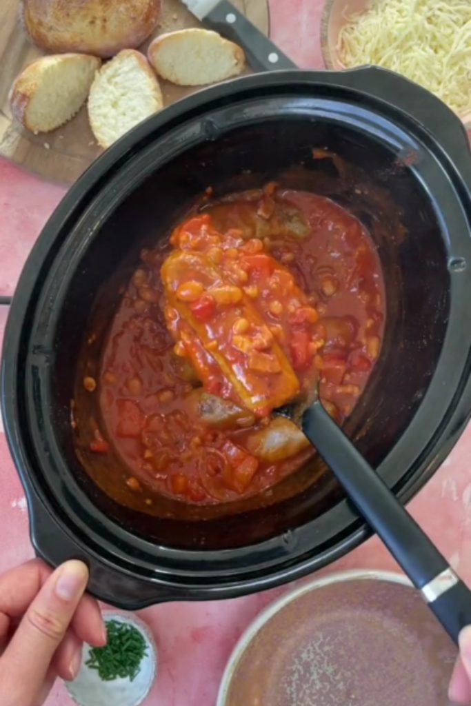 Sausage and baked bean casserole in a slow cooker with bread on the side.