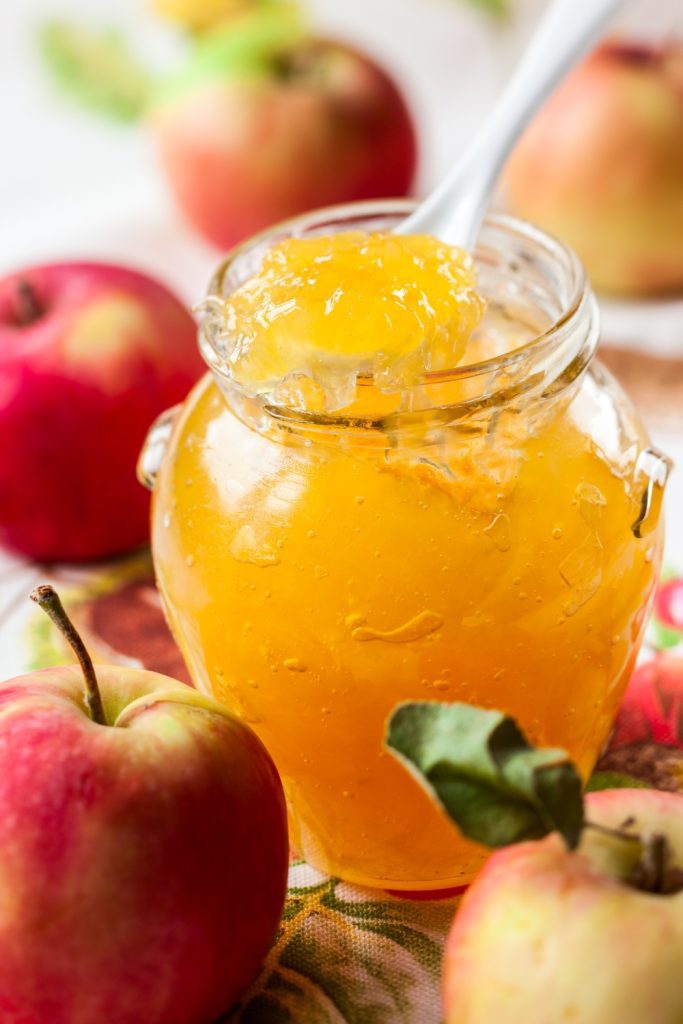 Bowl of apple jam with apples and cinnamon sticks around.