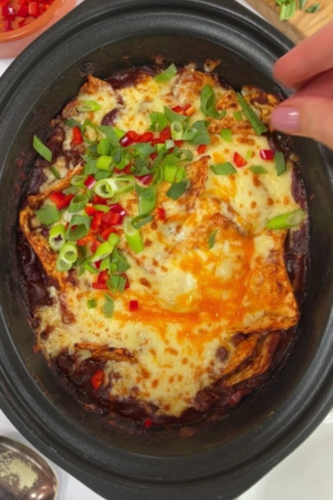 Slow Cooker Beef Enchilada Casserole with melted cheese and chopped green onions and red peppers.