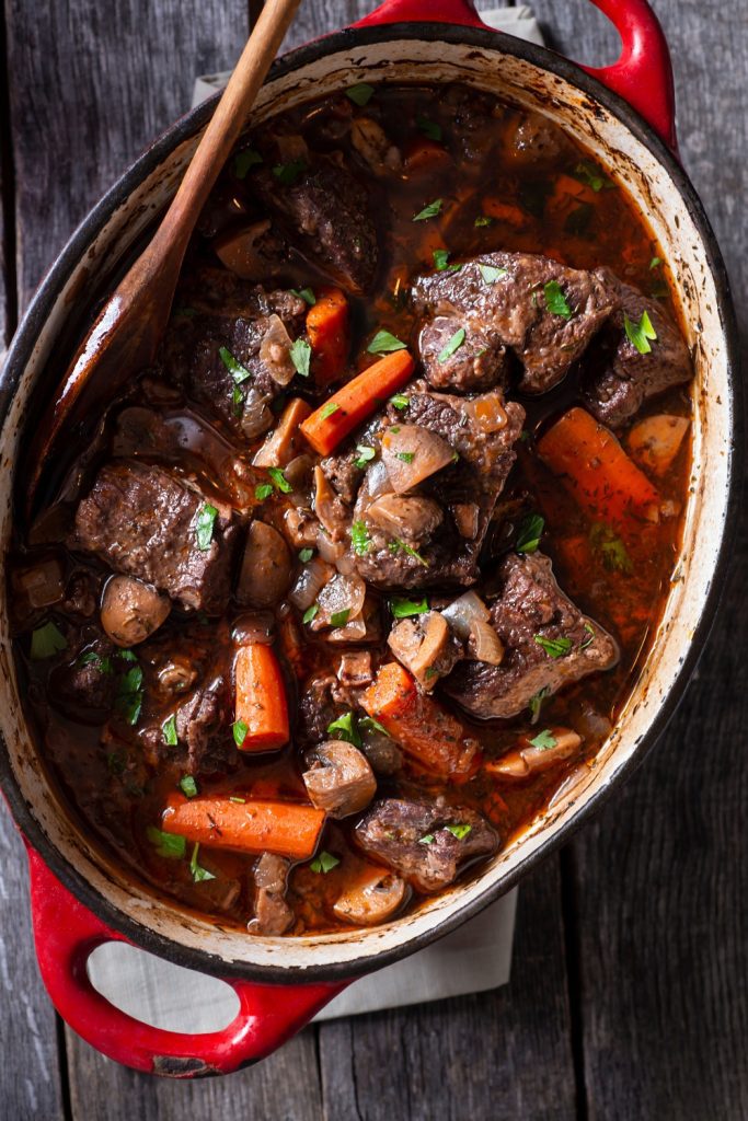 Beef and Red Wine Casserole with carrots and mushrooms in a red dish.