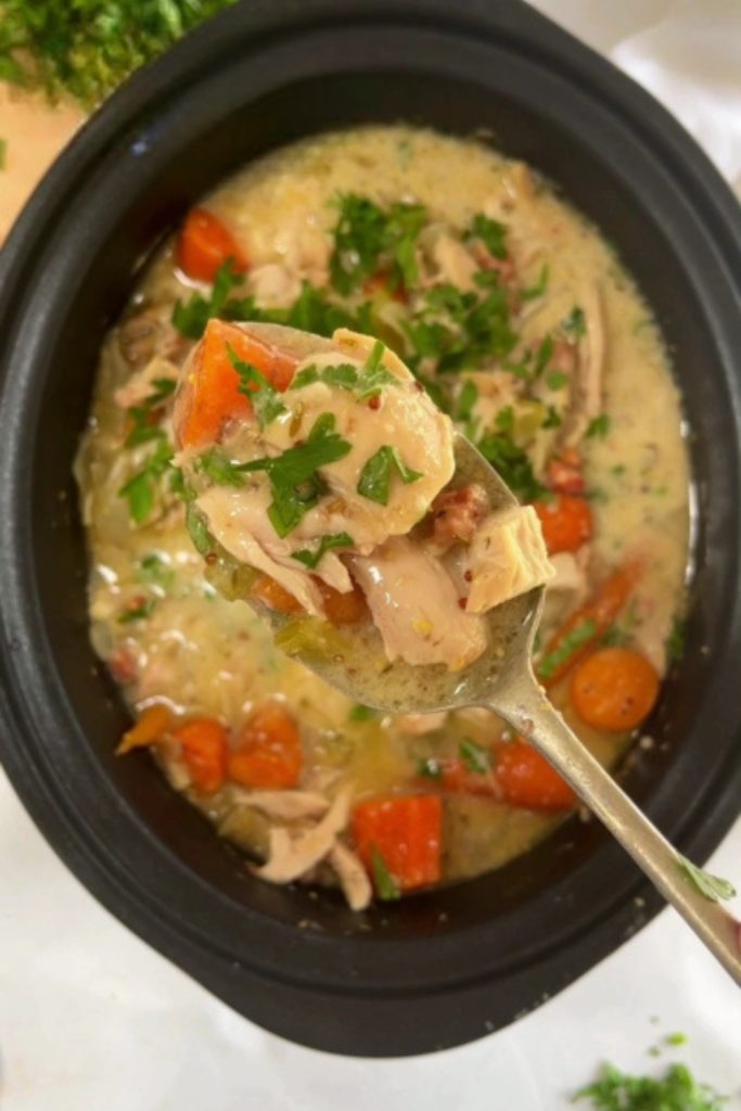 Slow Cooker Chicken and Bacon Casserole with carrots and parsley, held on a spoon.