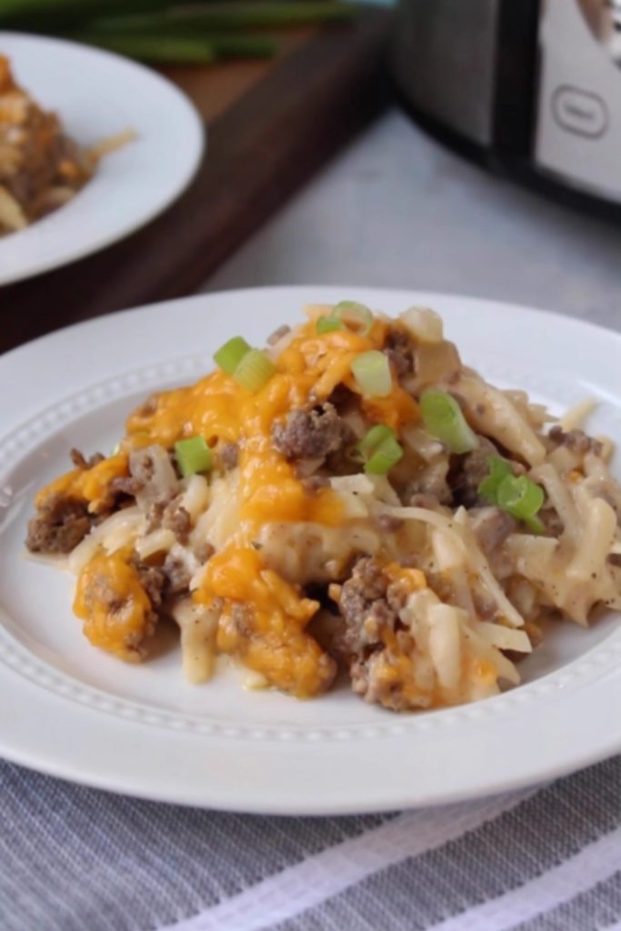 Slow Cooker Hamburger Hash Brown Casserole topped with melted cheese and green onions on a white plate.