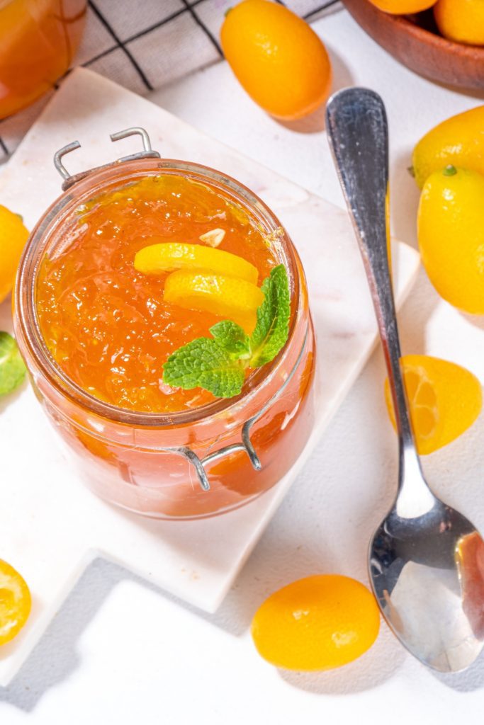 Jar of kumquat jam with fresh kumquats and mint garnish.