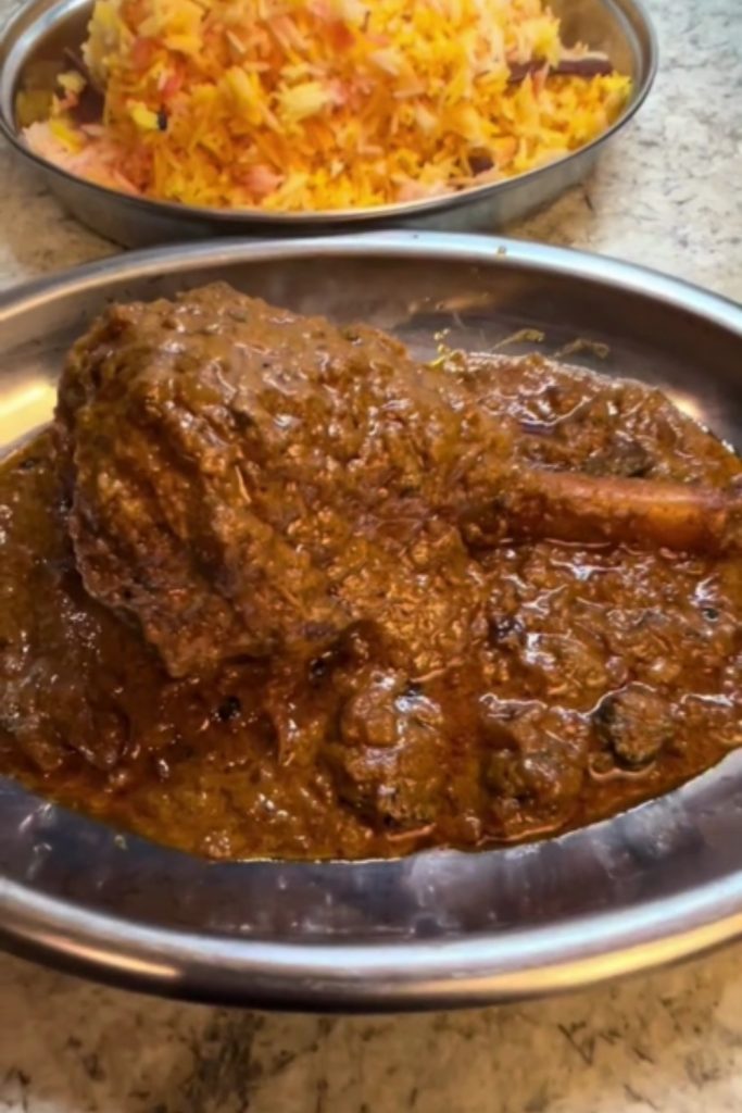 Slow Cooker Lamb Shank Rogan Josh served in a metal bowl with a side of saffron rice.