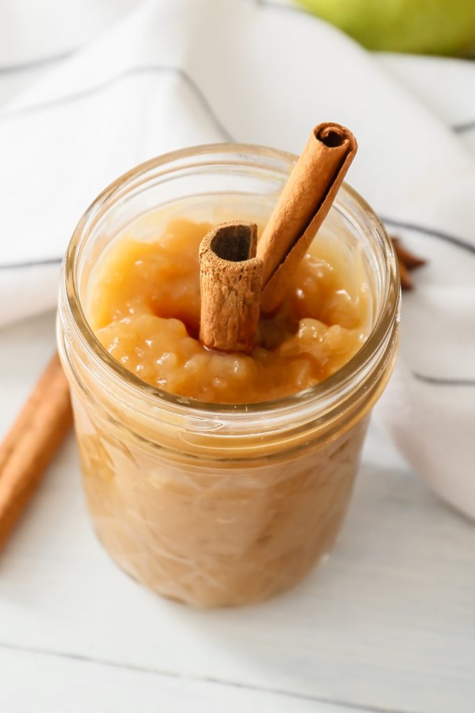 A jar of Slow Cooker Pear Jam with a cinnamon stick on top.