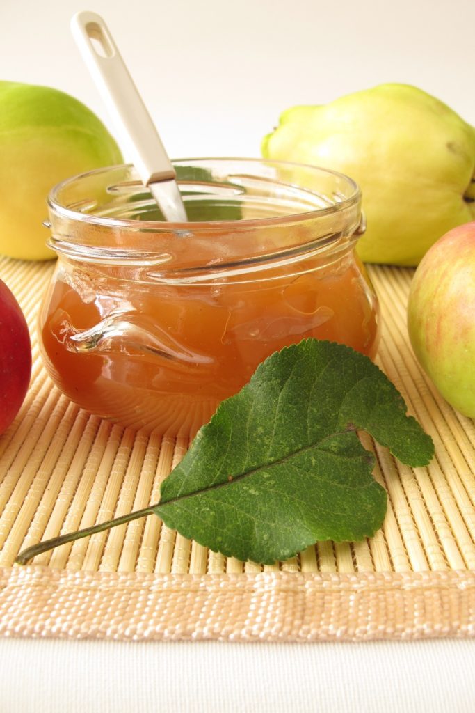 Quince jam in a jar with fresh quince and leaves.