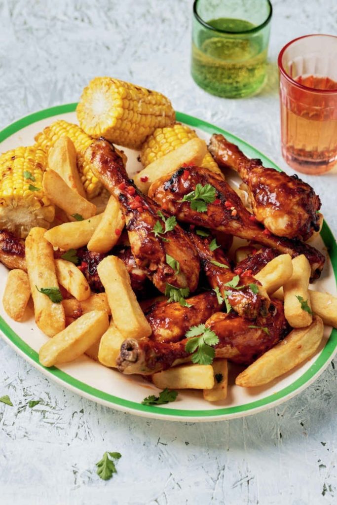 Slow Cooker Spicy Chicken Drumsticks with fries and corn on a white plate with a green rim.