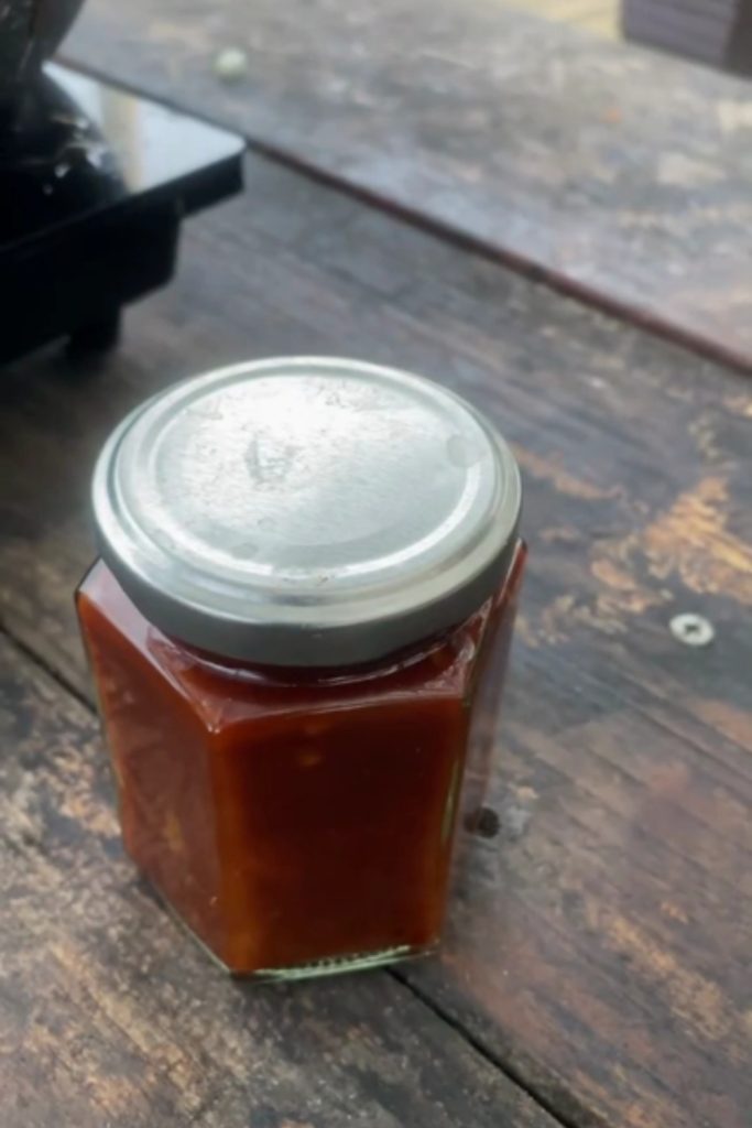 Tomato Capsicum Relish in a closed jar on a wooden surface.
