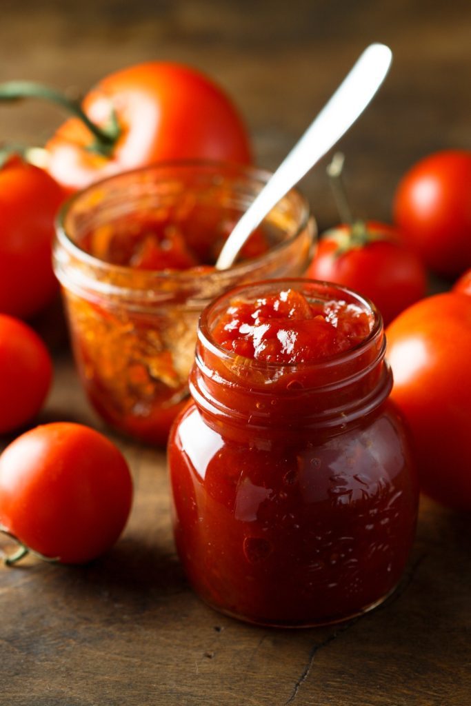 A jar of Slow Cooker Tomato Jam with fresh tomatoes in the background.