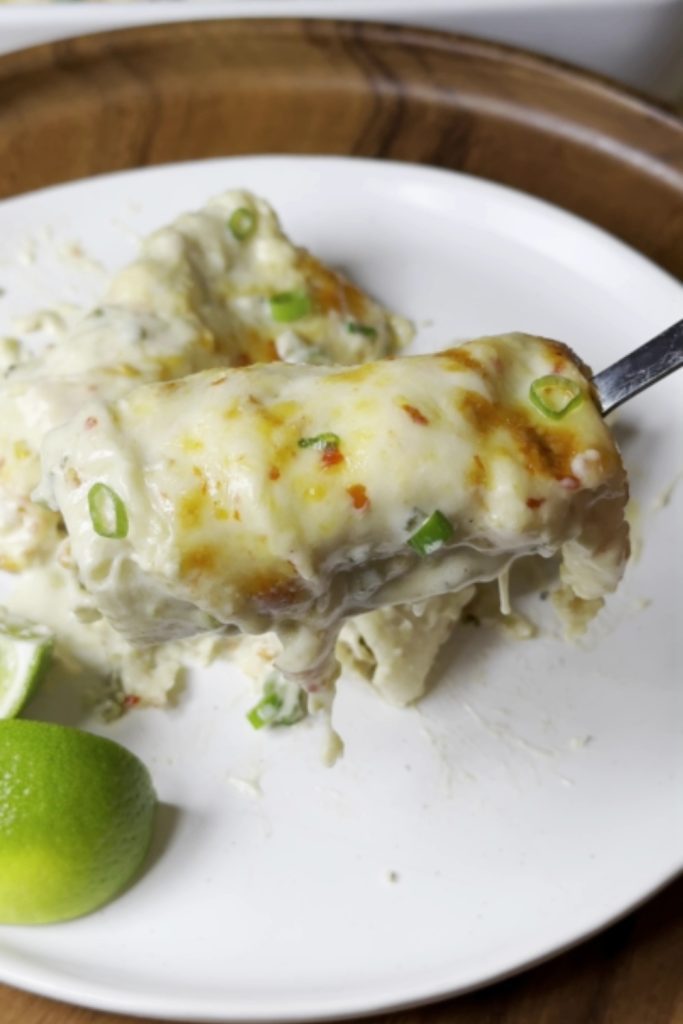 White Chicken Enchilada topped with cheese and green onions on a fork with lime on the side.