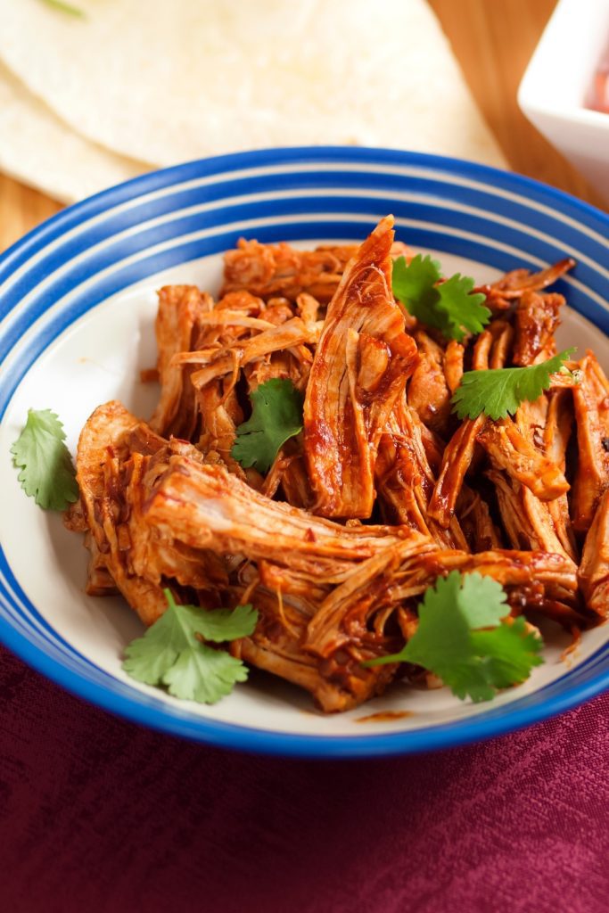 Shredded pulled pork in a blue and white bowl, garnished with fresh cilantro.