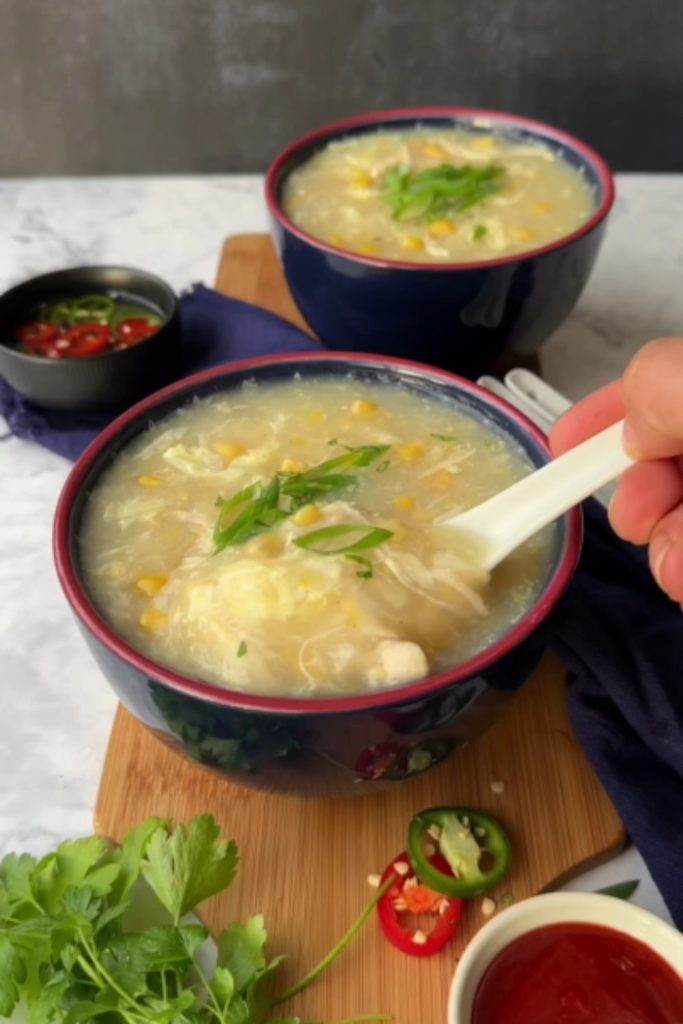 A bowl of 4 Ingredients Slow Cooker Easy Chicken and Corn Soup, garnished with green onions, with a spoon lifting a portion.