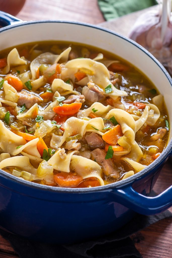 Chicken noodle soup with vegetables in a blue pot.