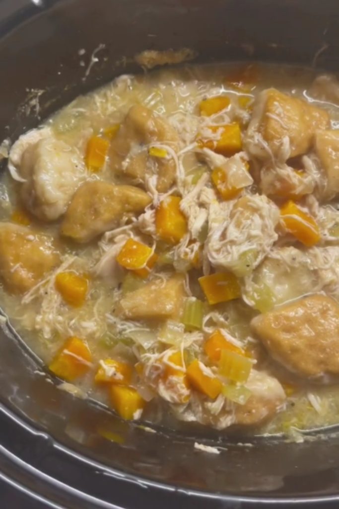 A crockpot filled with 5 Ingredient Chicken and Dumplings, featuring shredded chicken, dumplings, carrots, and celery in a thick broth.