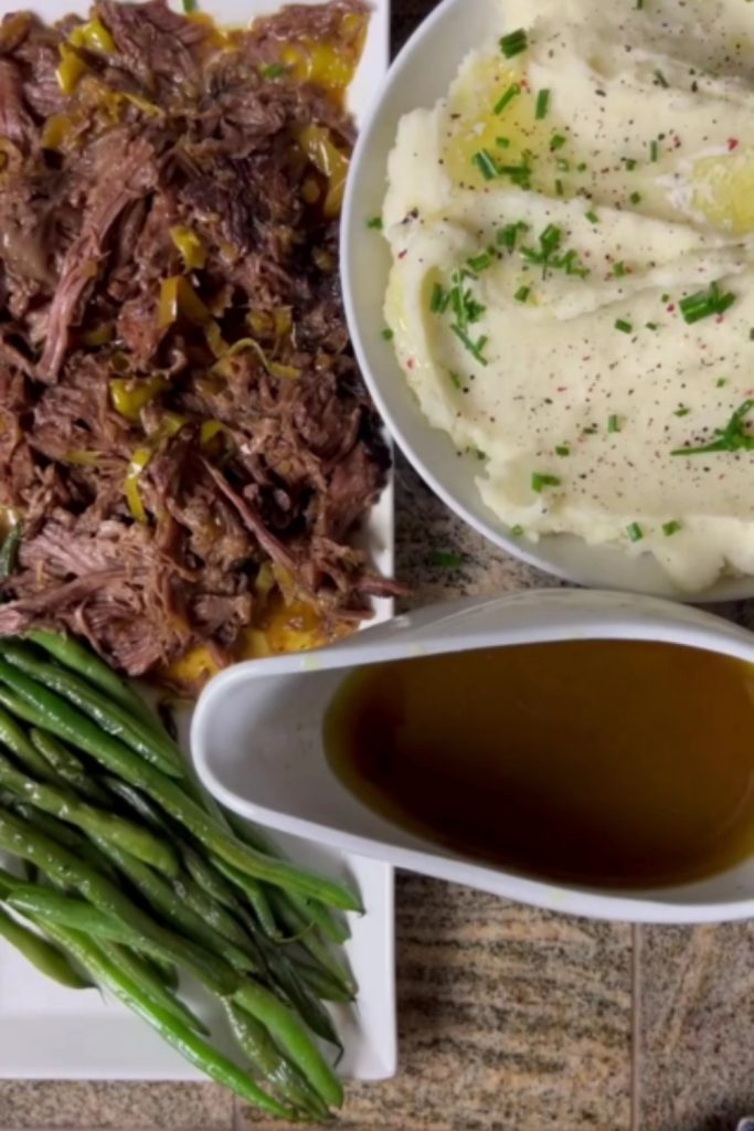 Slow Cooker Mississippi Pot Roast with mashed potatoes, green beans, and gravy on a white plate.