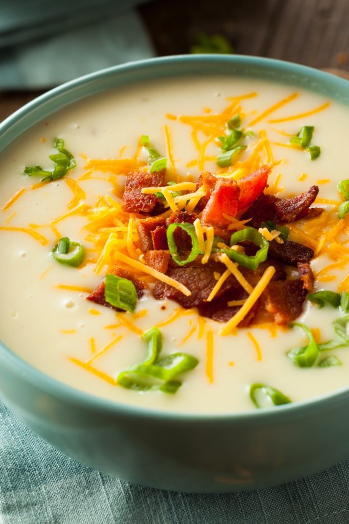 Creamy potato soup topped with bacon, cheese, and green onions in a blue bowl.