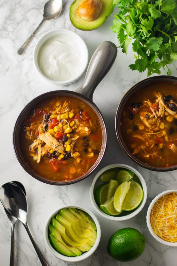  Two bowls of chicken tortilla soup with toppings on a marble surface.