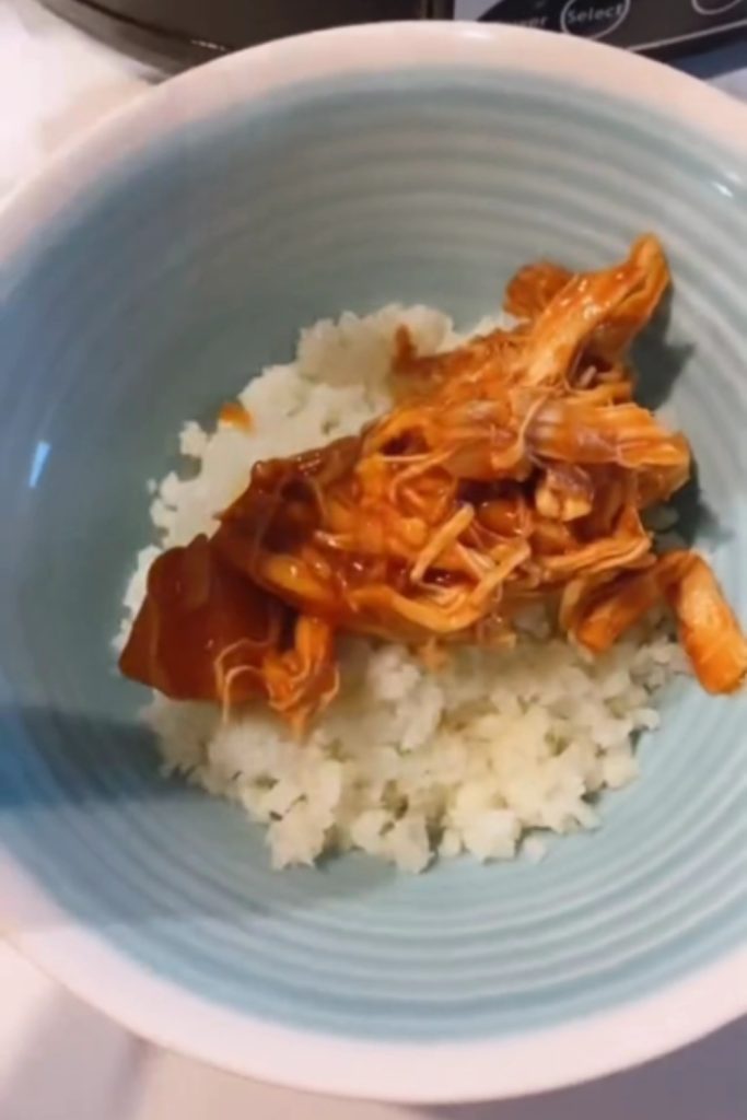 Shredded chicken with sauce over cauliflower rice in a blue bowl.