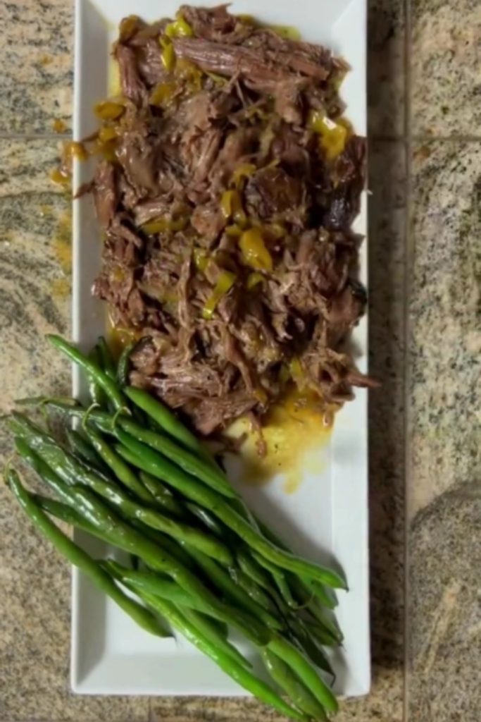 Shredded Slow Cooker Mississippi Pot Roast with green beans on a white rectangular plate.