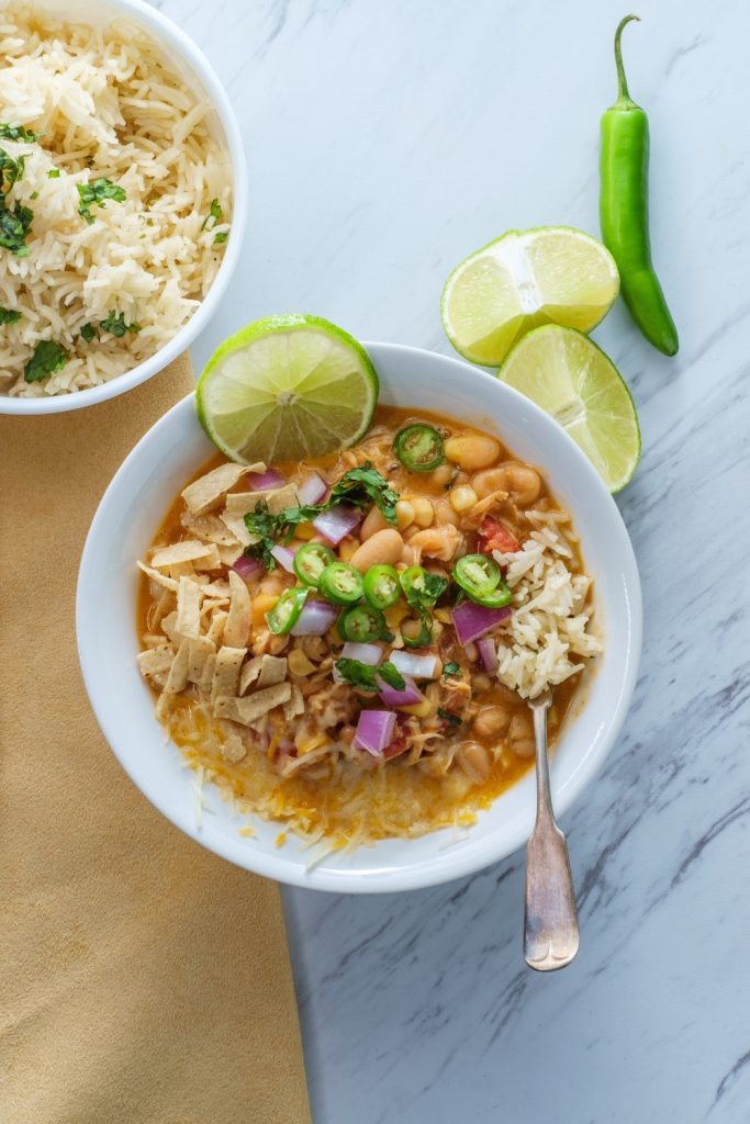 White chicken chili in a bowl with lime, tortilla strips, and sliced jalapenos.