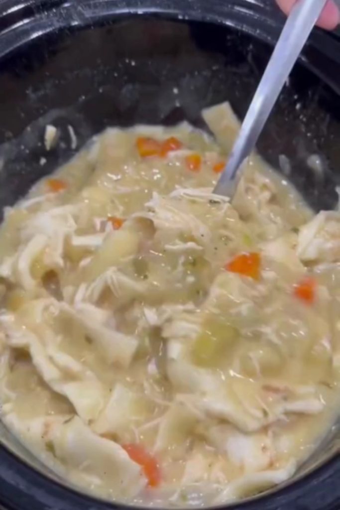 A crockpot filled with chicken and dumplings, showing shredded chicken and vegetables in thick gravy.