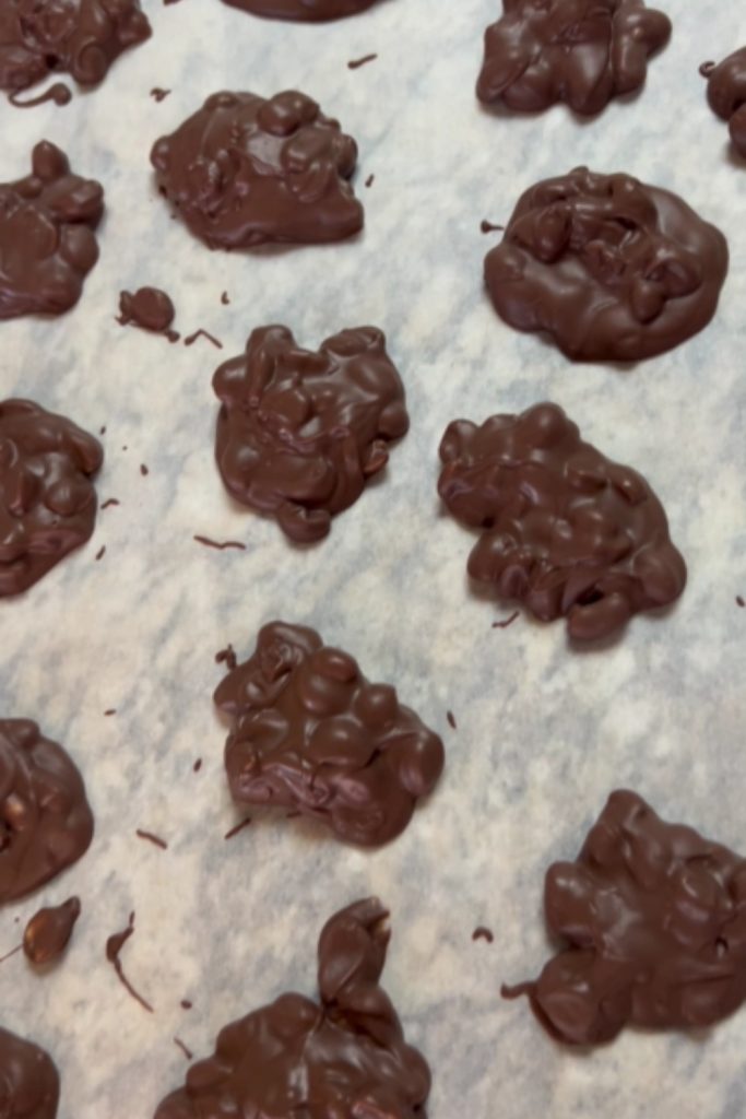 Chocolate peanut clusters setting on parchment paper.