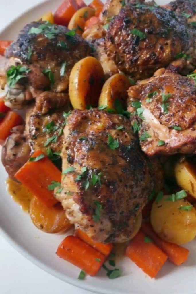 Balsamic chicken thighs and vegetables garnished with herbs on a white plate.