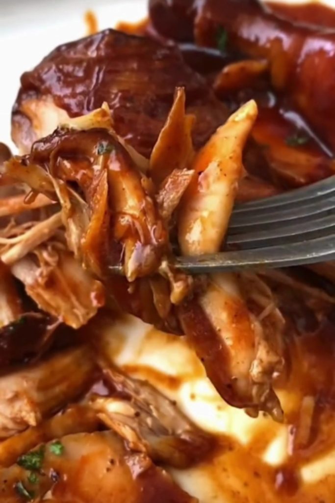 shredded chicken legs in a rich sauce on a fork.