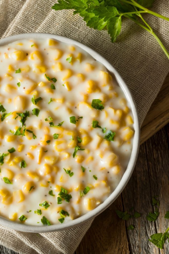 creamed corn garnished with parsley in a white bowl.