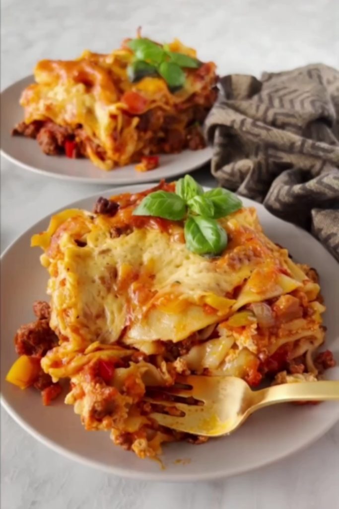 lasagna slice on a plate with basil on top.