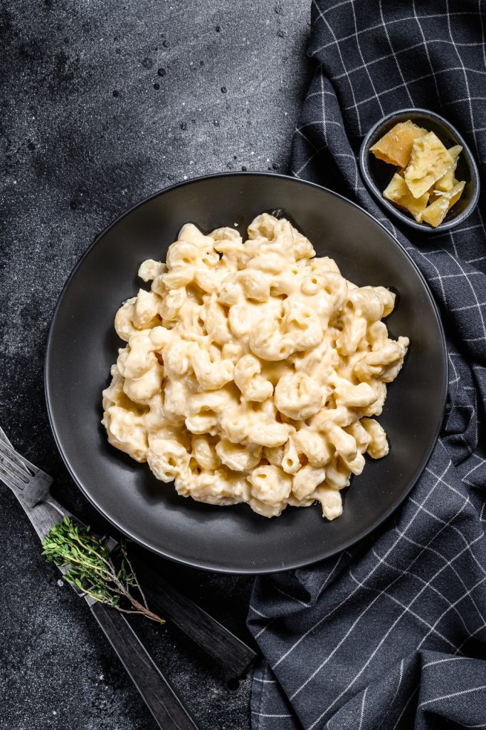 A black bowl filled with creamy 5 Ingredient Slow Cooker Mac and Cheese on a dark surface, with a small bowl of cheese pieces on the side.