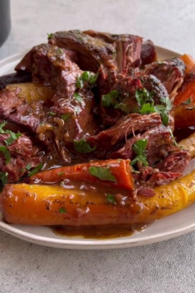 Pot roast with carrots garnished with parsley on a white plate.