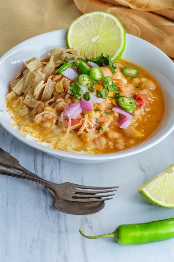 Bowl of white chicken chili with rice, lime, and jalapenos on a marble surface.